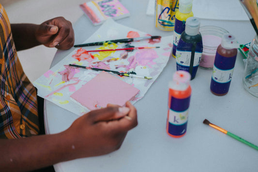 hands engaged in a shared painting activity with art supplies spread across the table.